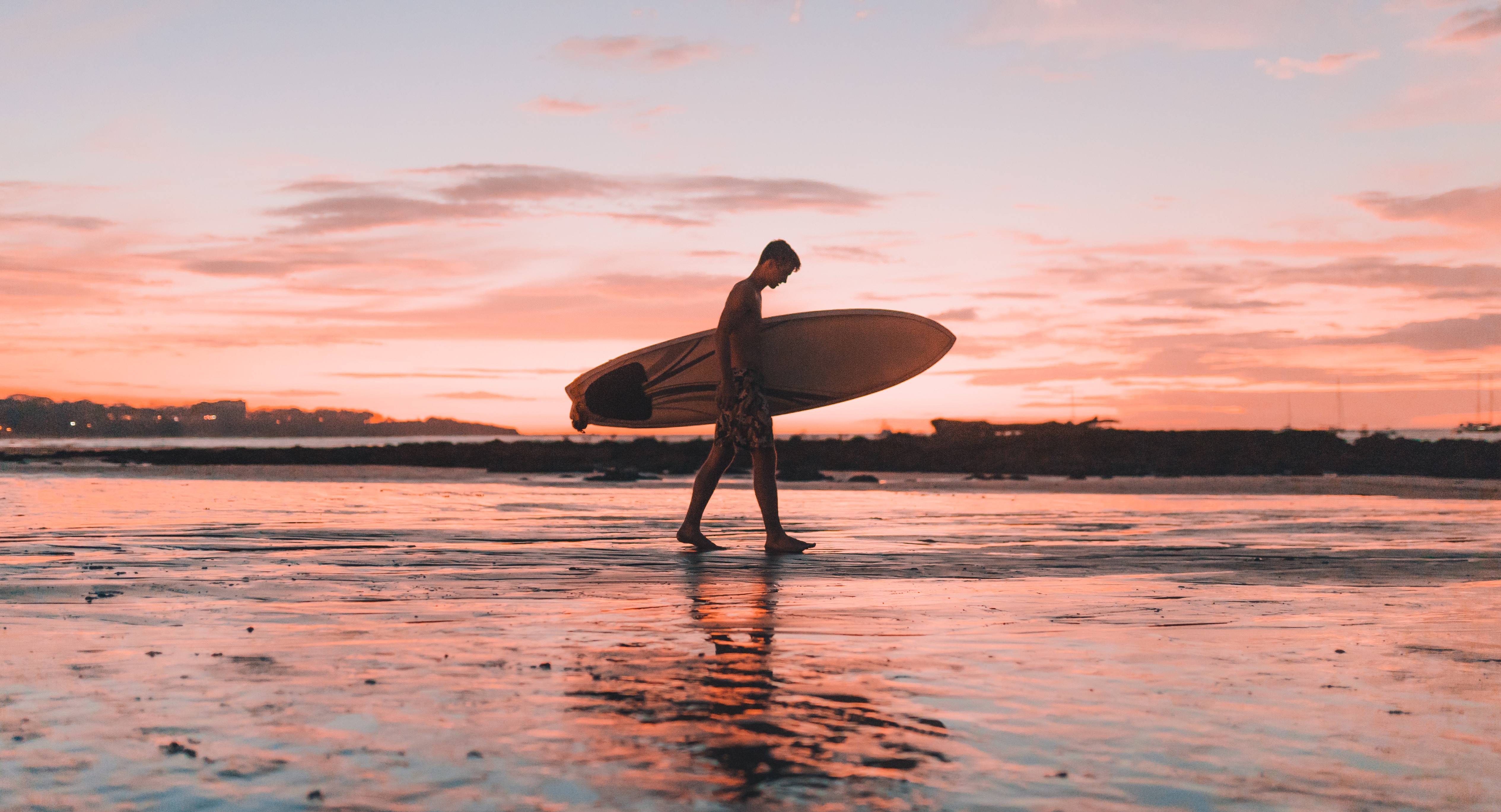 Een surfer bij zonsondergang op het strand van Tamarindo, Costa Rica