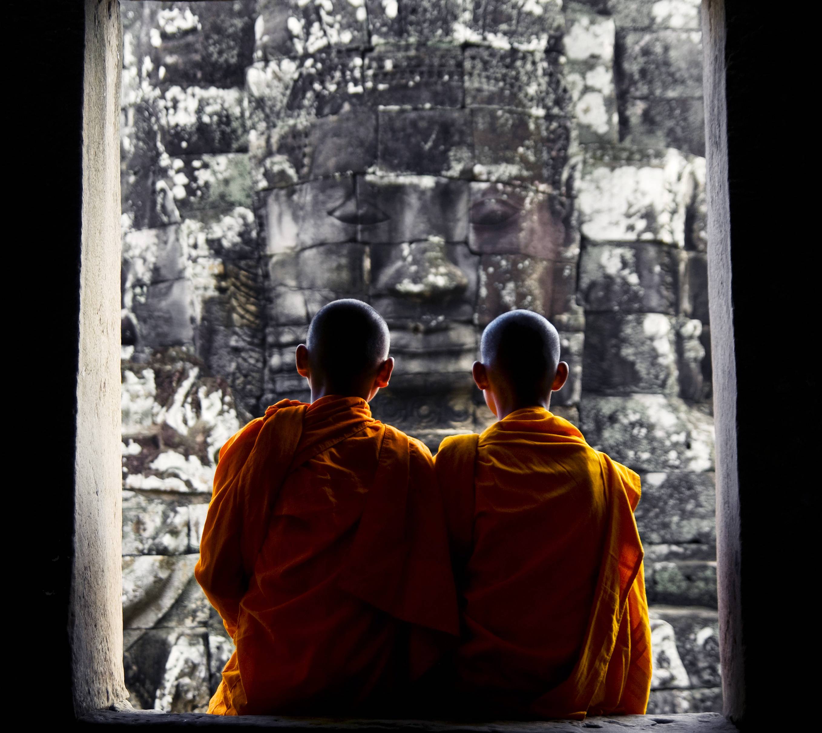 Twee monniken zitten in een raamopening te kijken naar Angkor Wat, Cambodja