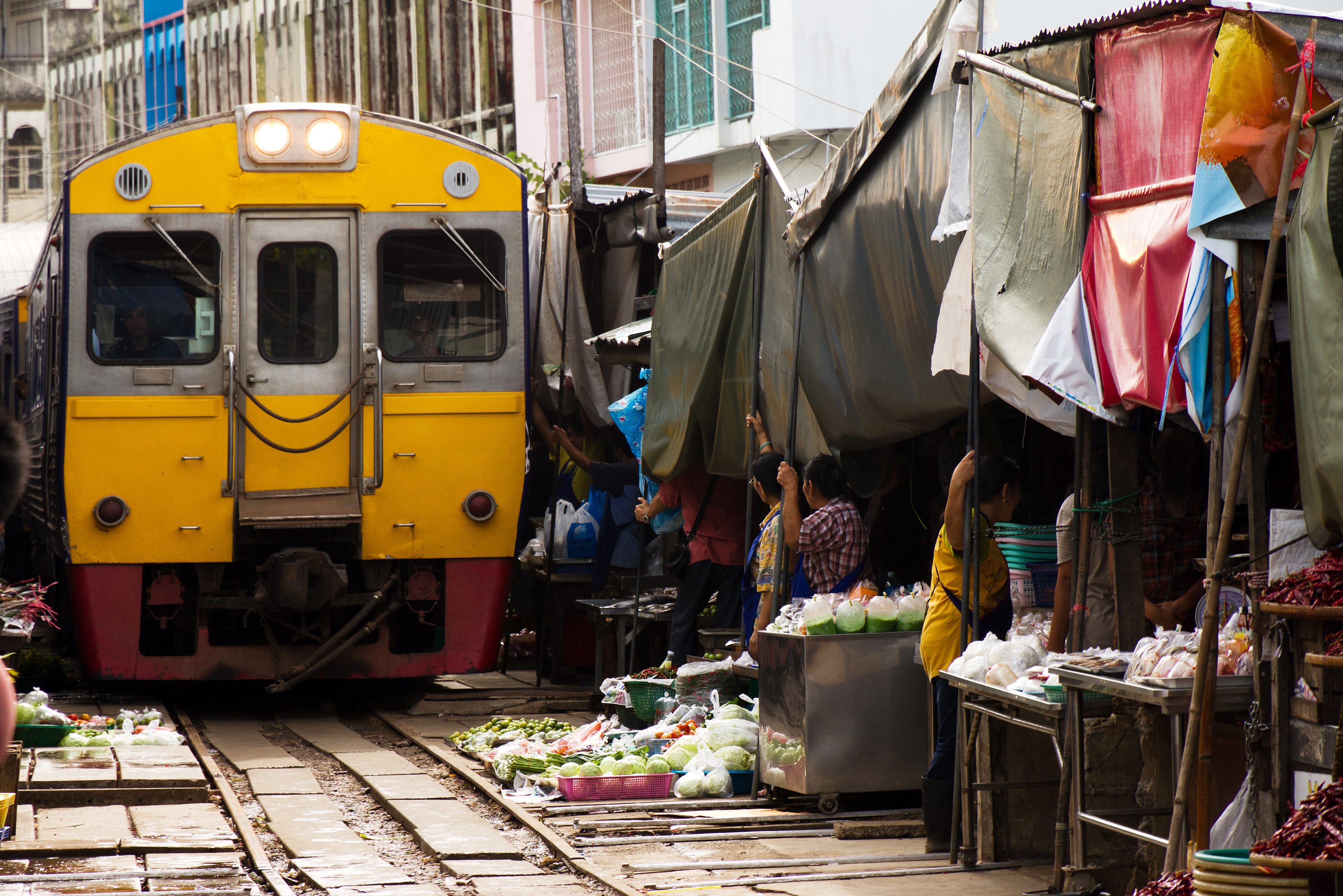 Trein rijdt vlak langs huizen en koopwaar in Thailand