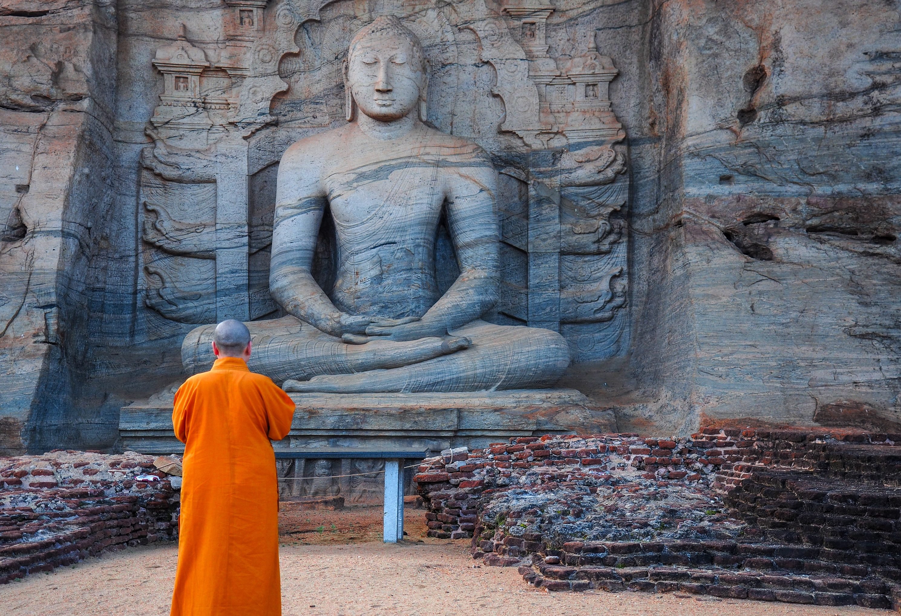 Monnik bij zittende Boeddha in Polonaruwa